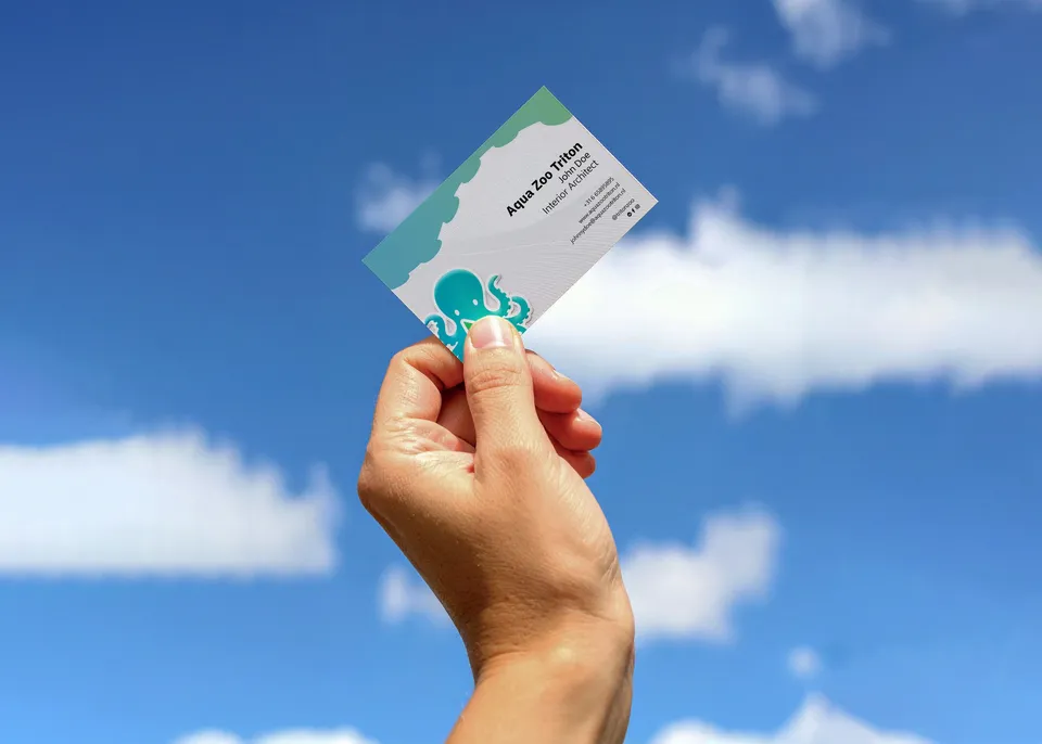 A hand holding an Aqua Zoo Triton business card against a blue sky with clouds.