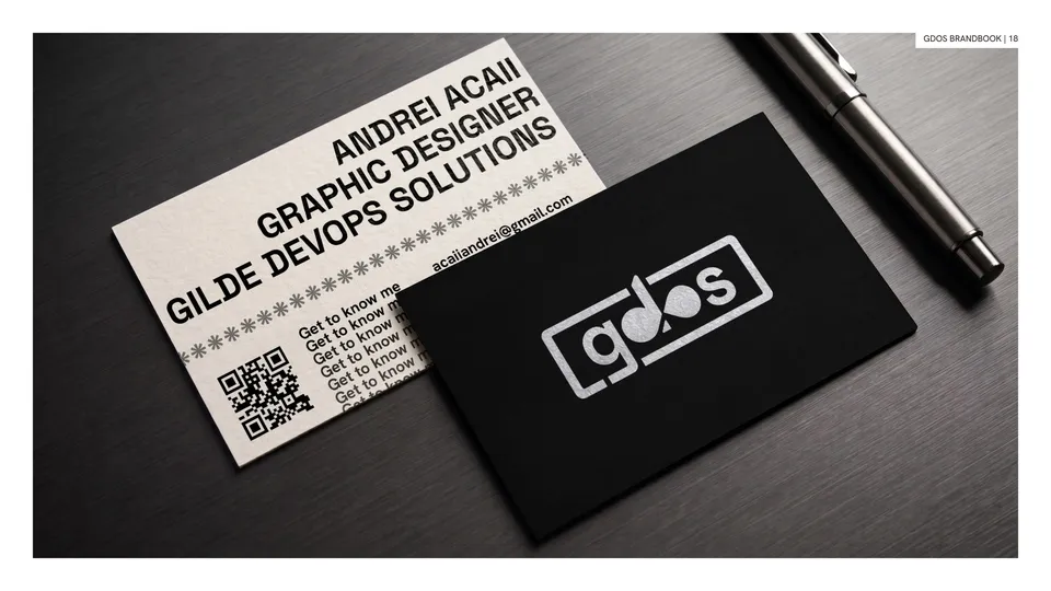 Black and white gdos business cards for Andrei Acaii lying on a dark surface next to a pen.