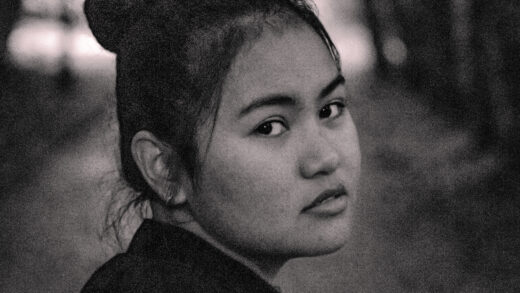 A photo of a filipina girl looking directly at the camera, serious look towards the camera, black and white photography, very grainy.