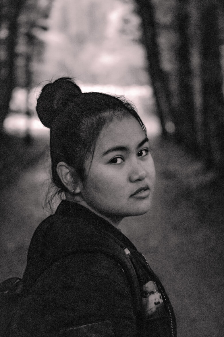 A photo of a filipina girl looking directly at the camera, serious look towards the camera, black and white photography, very grainy.