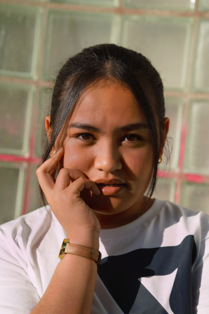 A photo of a filipina girl looking directly at the camera, posing with a smug face, hand on her left cheek.