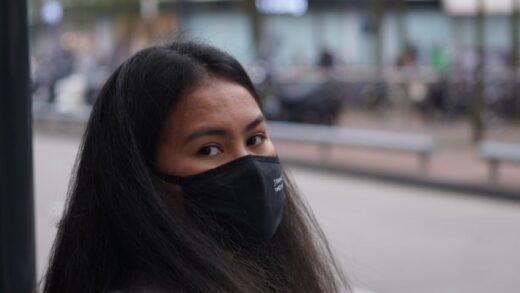 A photo of a filipina girl looking directly at the camera, with a mask covering her mouth, with a sad look on her face, about to leave for the bus.